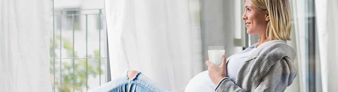 Pregnant woman sitting at the window drinking a glass of milk