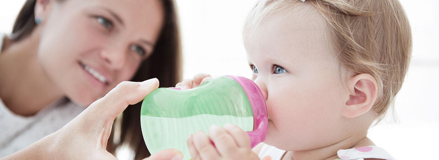 A toddler drinks baby food from Babina out of a cup