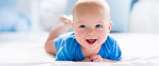 A baby is lying on the bed laughing