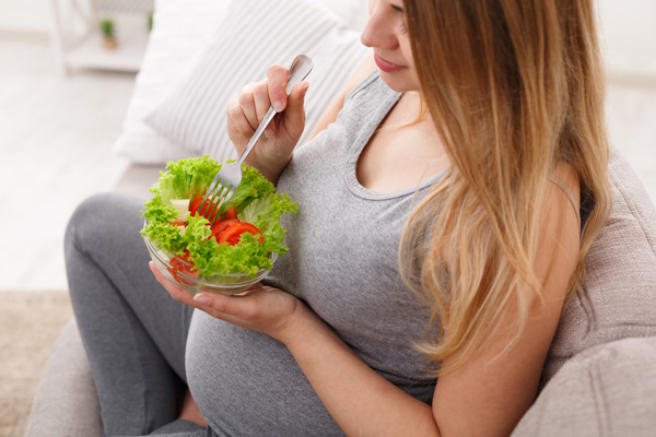 Mujer embarazada está comiendo ensalada 